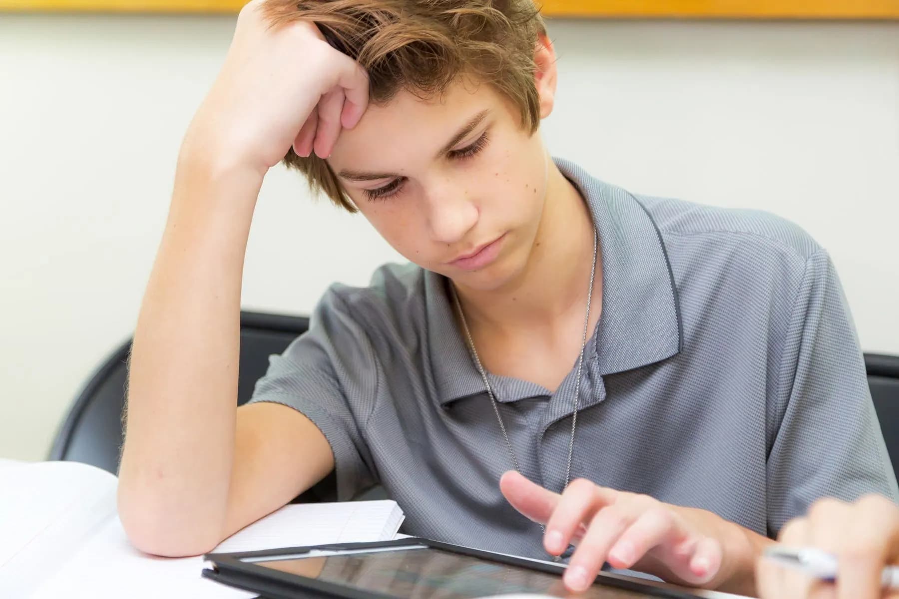 Student using a tablet in a classroom for learning requirements.