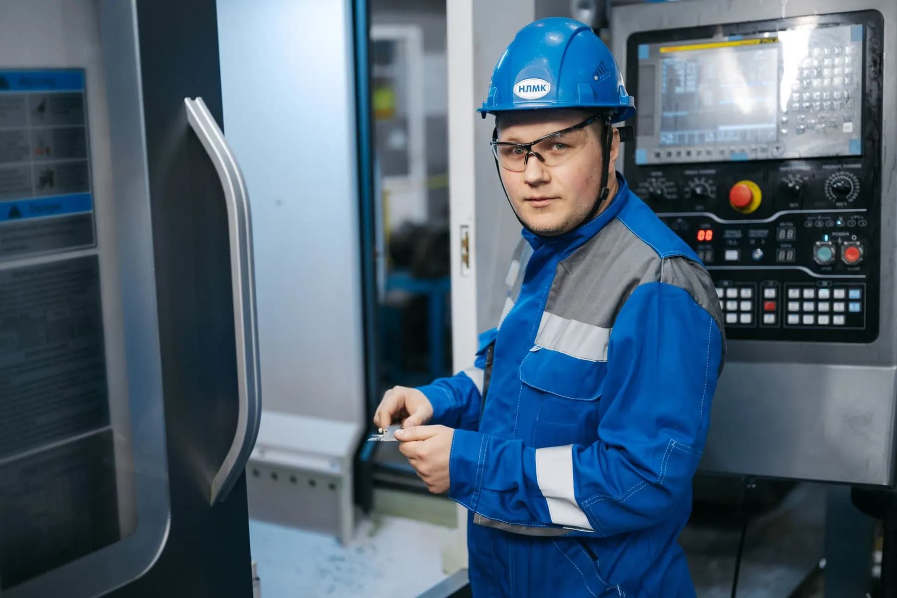 Industrial engineer operating CNC machinery while reviewing technical requirements.