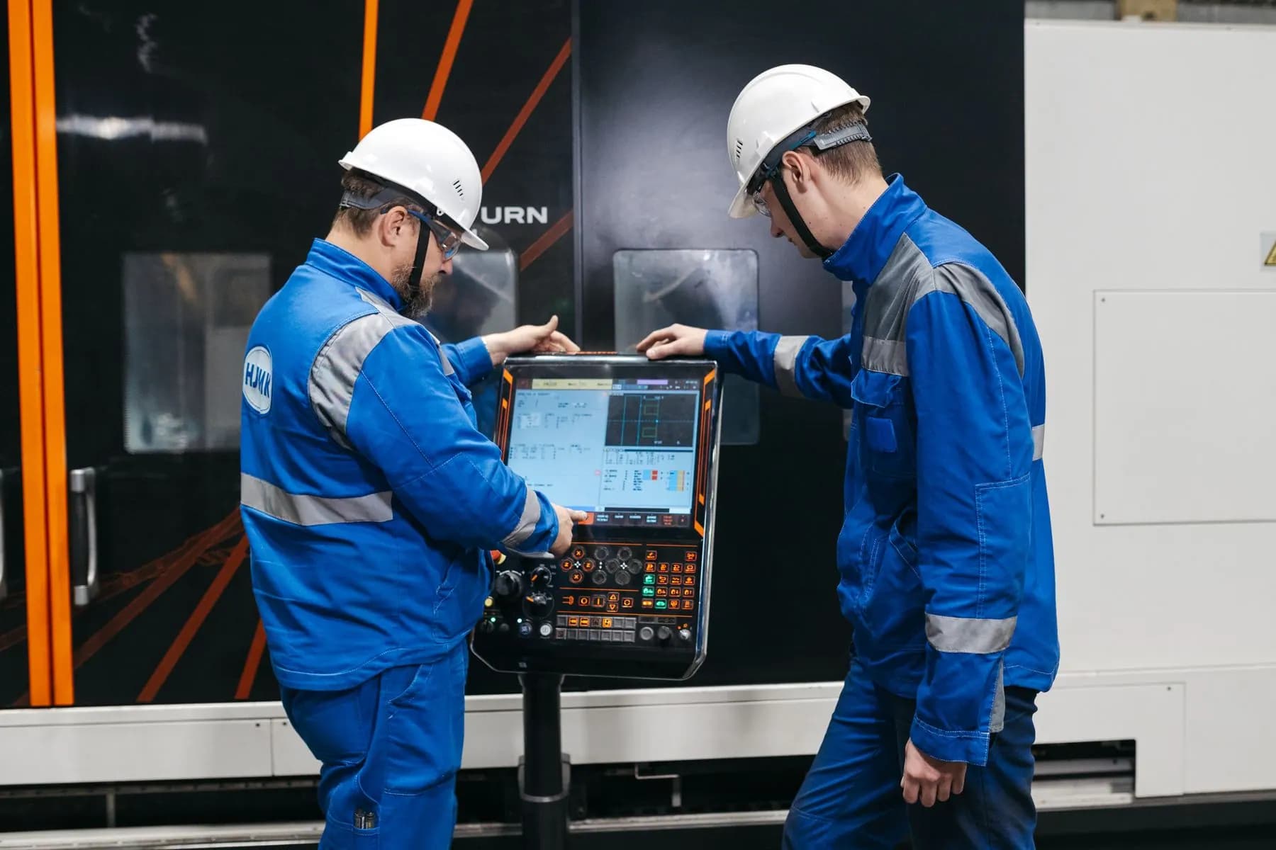 Two engineers operating CNC machinery for technical and commercial comparison.